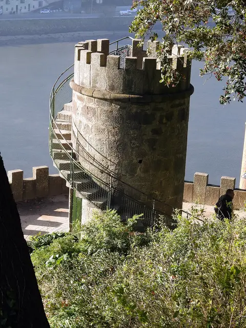 Torre de pedra ameada com escada em caracol junto ao rio, num miradouro rodeado de vegetação
