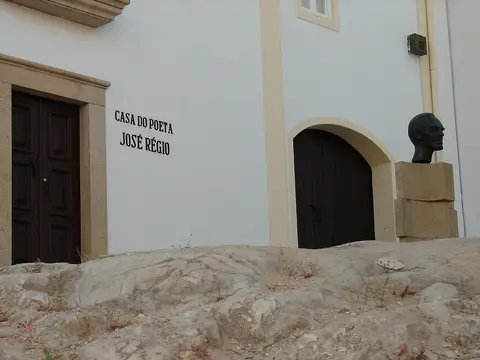Fachada branca da Casa do Poeta José Régio com letreiro, portas de madeira e busto em bronze