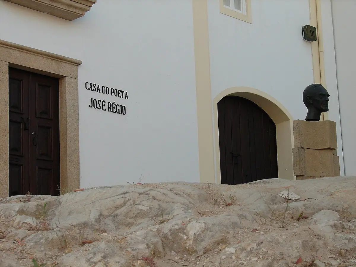 Fachada branca da Casa do Poeta José Régio com letreiro, portas de madeira e busto em bronze
