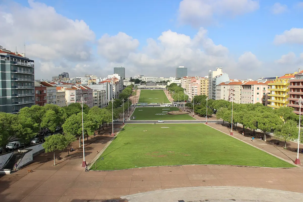 Vista elevada da Alameda Dom Afonso Henriques, com relvados, árvores e prédios em redor, em Lisboa