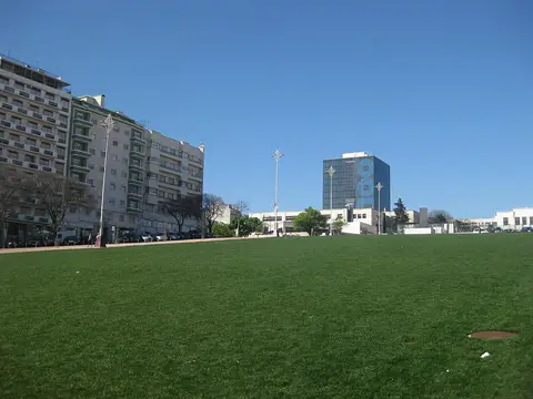 Grande relvado da Alameda Dom Afonso Henriques em Lisboa, com prédios e edifício envidraçado ao fundo