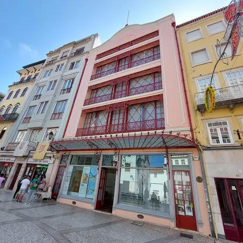 Fachada rosa do Edifício Chiado em Coimbra, com varandas de ferro e montras ao nível da rua.