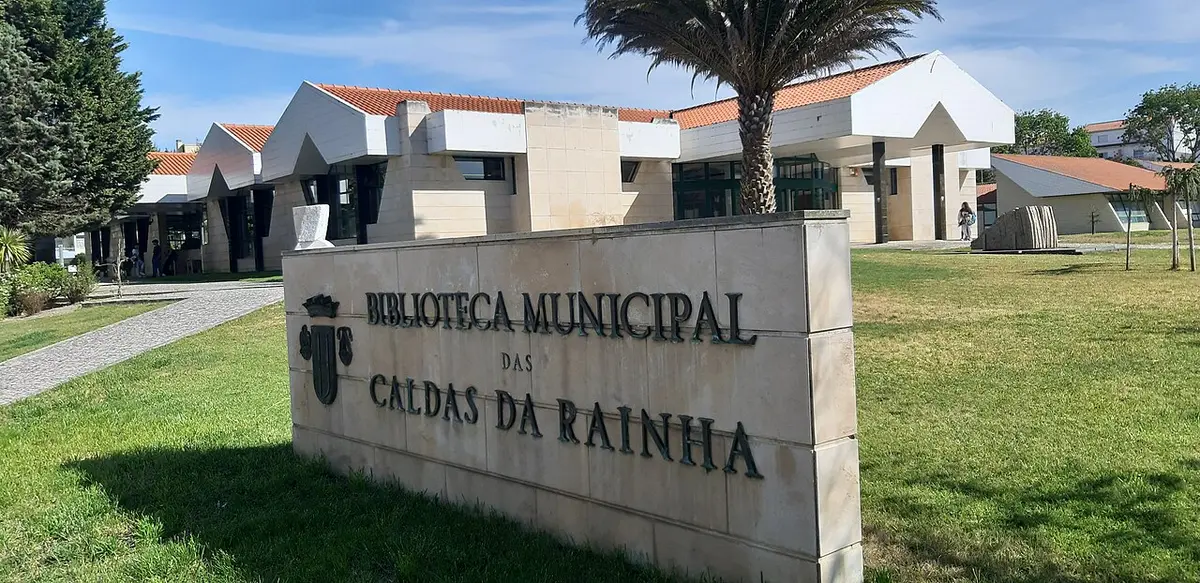 Letreiro em pedra da Biblioteca Municipal das Caldas da Rainha, com o edifício e jardim ao fundo