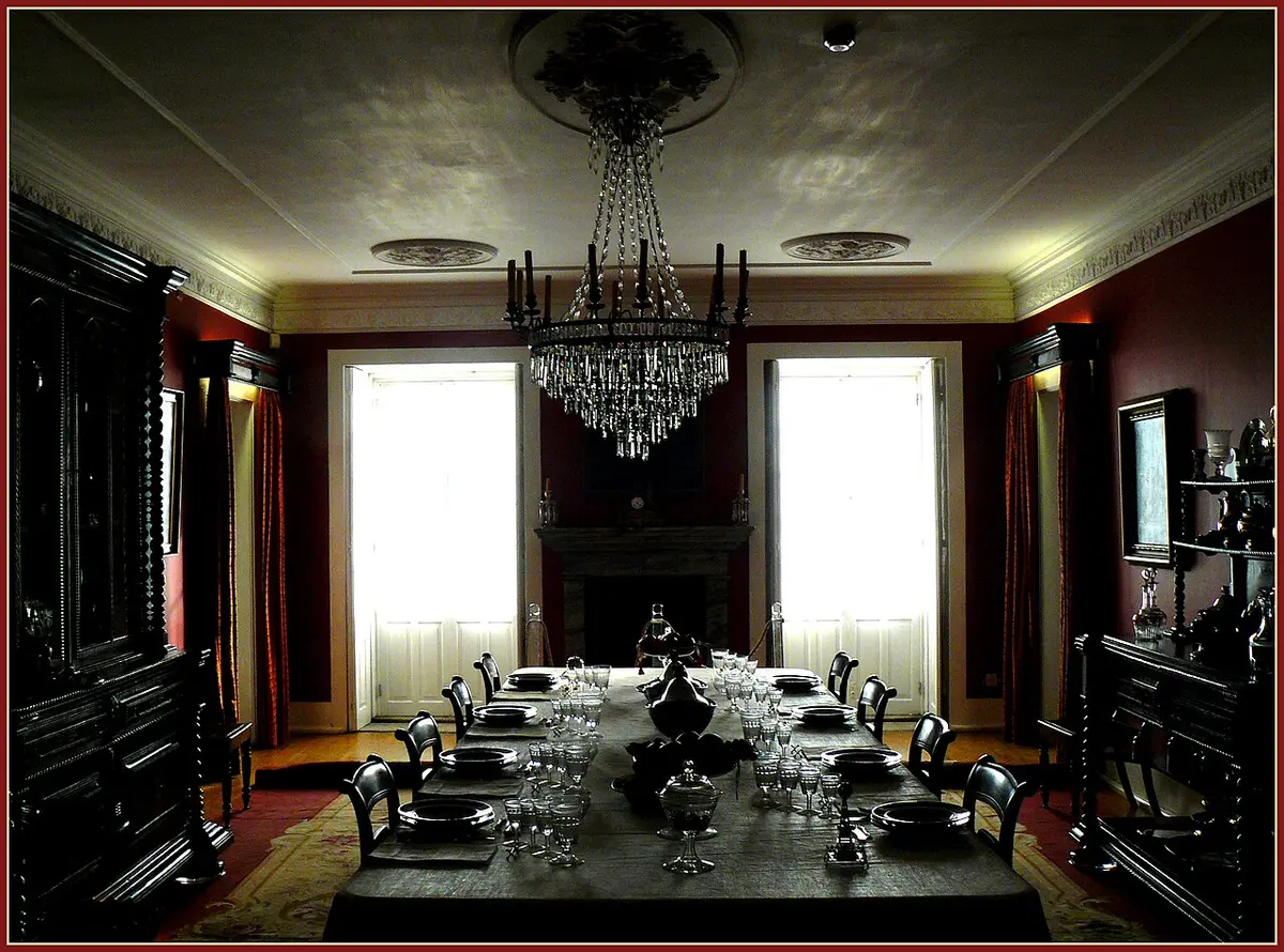 Sala de jantar do Museu do Romântico, com mesa posta, lustre de cristal e paredes vermelhas.