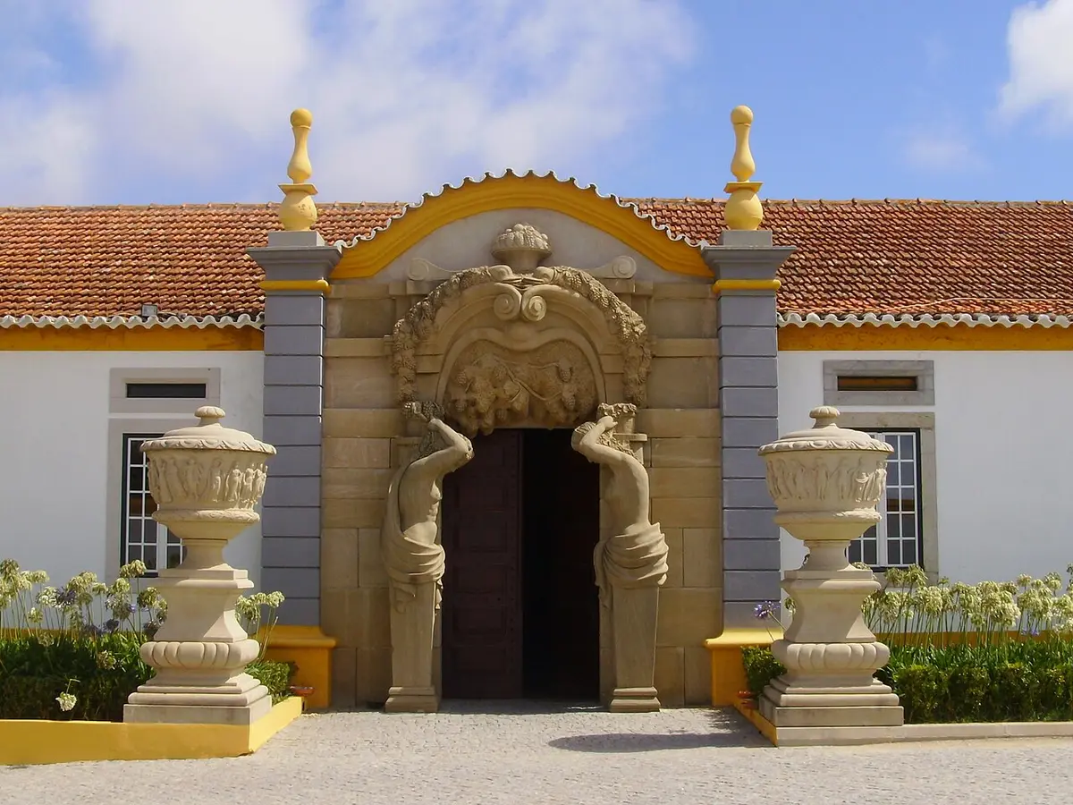 Portal barroco em pedra com estátuas e urnas decorativas à entrada da Quinta dos Loridos