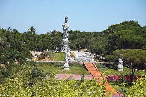 Jardim Buddha Eden com estátua branca alta, Buda reclinado e escadaria vermelha entre relvados e árvores