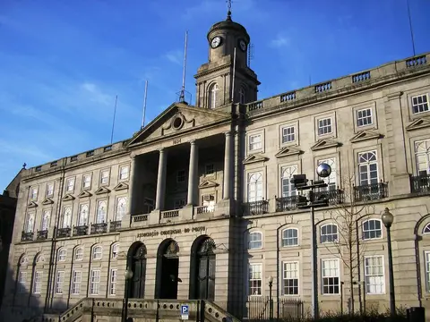 Fachada neoclássica do Palácio da Bolsa no Porto, com torre do relógio e céu azul