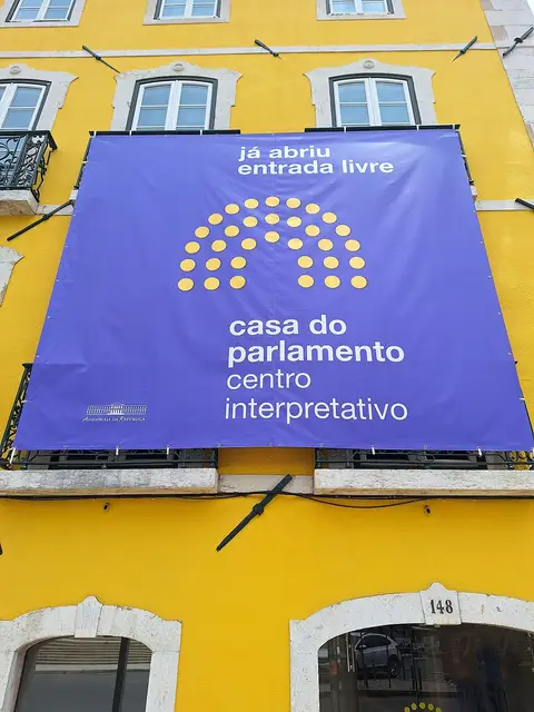 Fachada amarela com lona roxa a anunciar a Casa do Parlamento – Centro Interpretativo