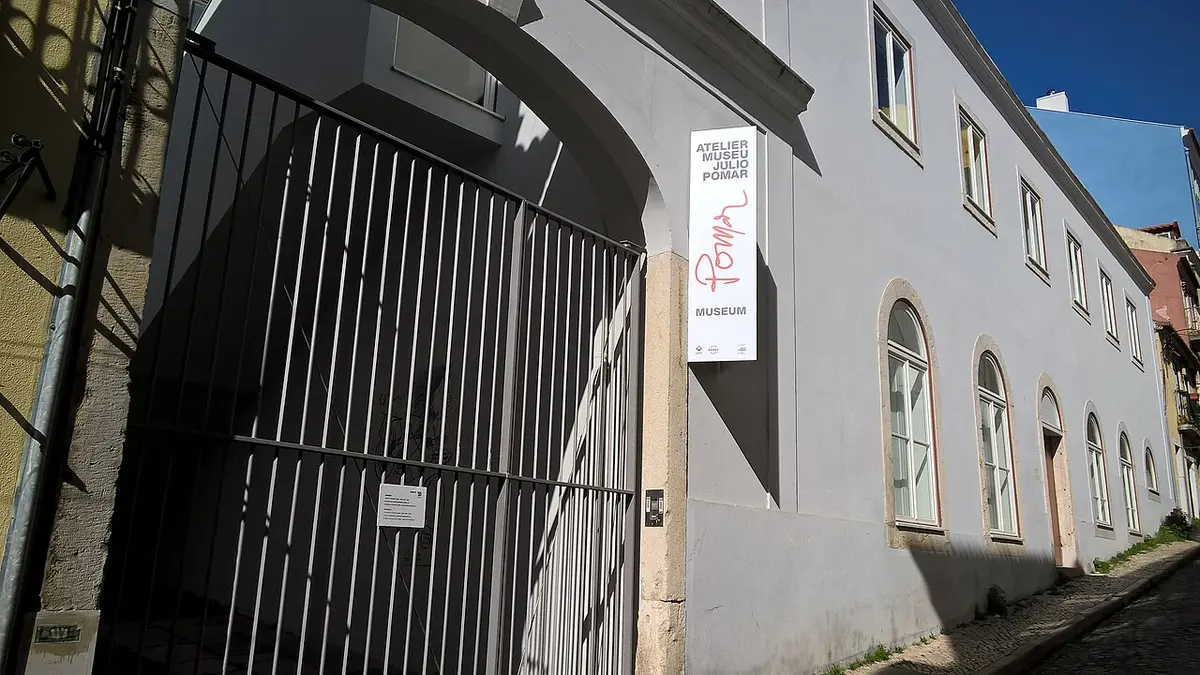 Entrada do Atelier-Museu Júlio Pomar, com portão de grades e letreiro vertical na fachada branca