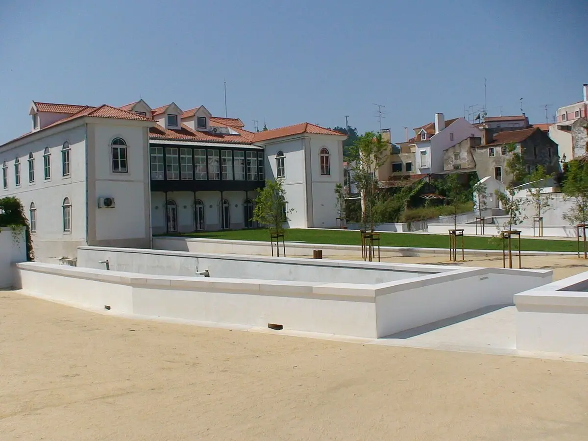 Edifício branco da Biblioteca Municipal de Alcobaça visto das traseiras, com esplanada e jardim