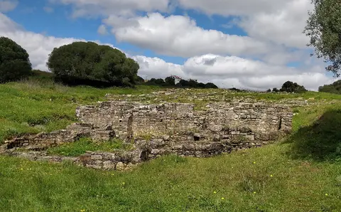 Ruínas de muros de pedra da Vila Romana de Freiria rodeadas de relva verde e céu com nuvens
