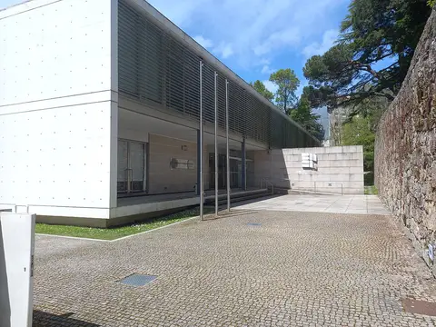Exterior moderno da Biblioteca Municipal Eduardo Lourenço, na Guarda, com pátio em calçada e muro de pedra.