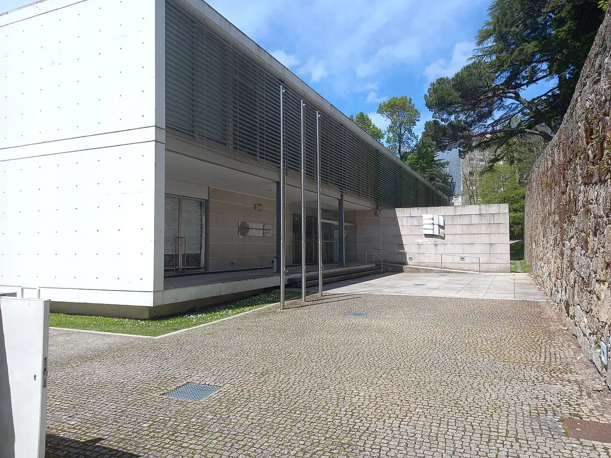 Exterior moderno da Biblioteca Municipal Eduardo Lourenço, na Guarda, com pátio em calçada e muro de pedra.
