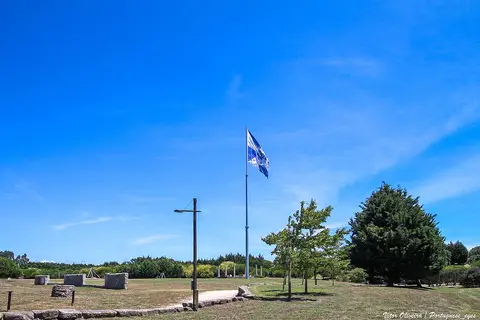 Relvado do Parque da Cidade da Póvoa de Varzim com mastro de bandeira e árvores sob céu azul