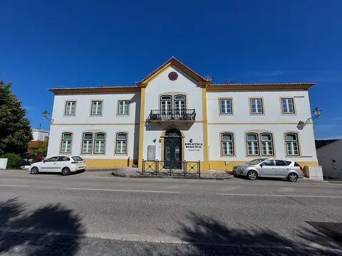Fachada branca e amarela da Biblioteca Municipal Alexandre O'Neill, em Constância, com carros estacionados