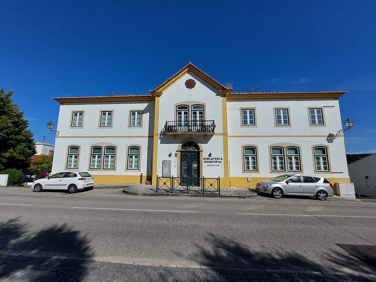 Fachada branca e amarela da Biblioteca Municipal Alexandre O'Neill, em Constância, com carros estacionados