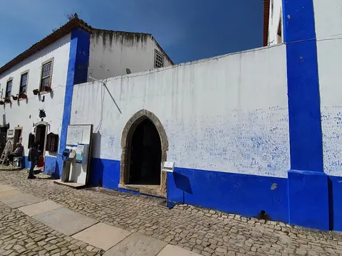 Fachada branca e azul da Biblioteca Municipal de Óbidos com porta em arco e rua de calçada