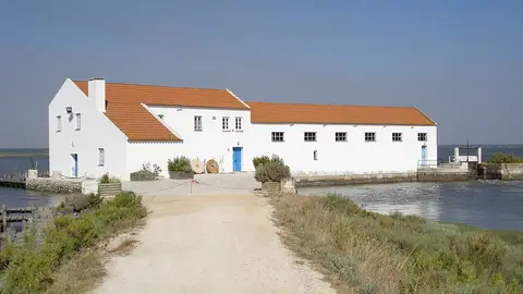 Moinho de Maré da Mourisca, edifício branco com telhado vermelho junto ao sapal e ao canal de água
