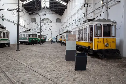 Interior do Museu do Carro Eléctrico com carros eléctricos antigos amarelos e verdes sobre calçada