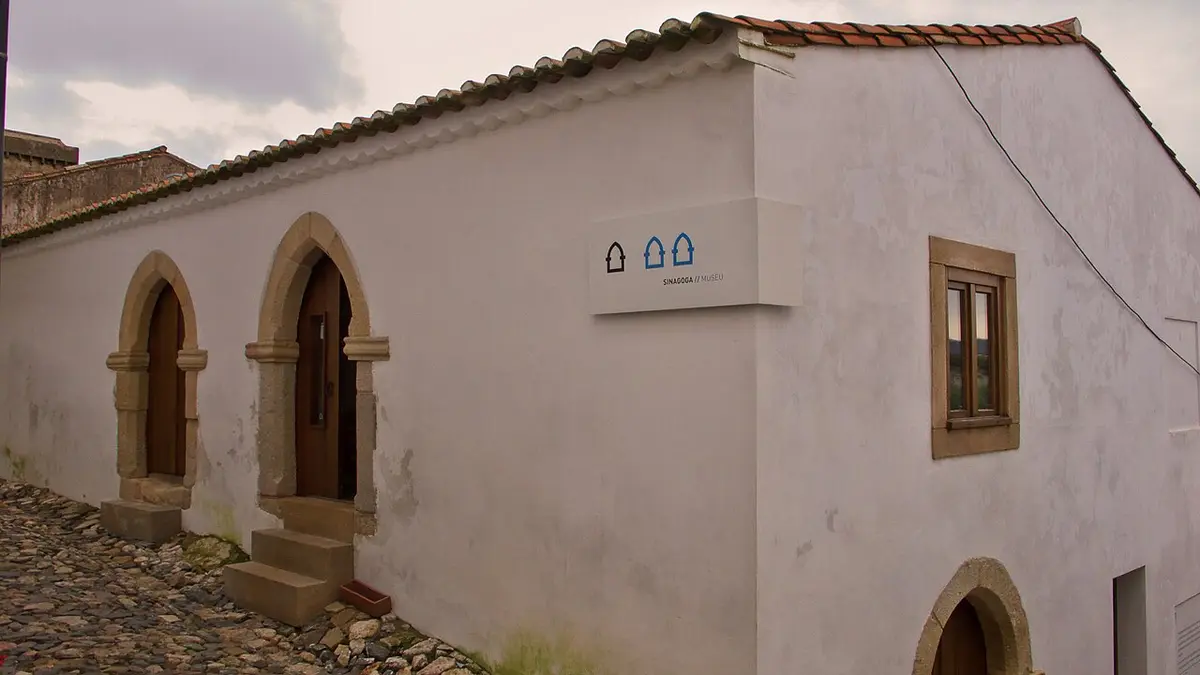 Exterior caiado da Sinagoga de Castelo de Vide, com portas em arco gótico e rua em calçada.