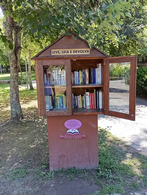 Armário de troca de livros em madeira num parque, com a inscrição «Leve, Leia e Devolva» e logótipo da Biblioteca Municipal Tomaz Ribeiro
