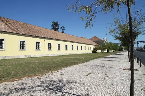 Fachada amarela comprida da Cordoaria Nacional, em Lisboa, junto a calçada portuguesa e relva.