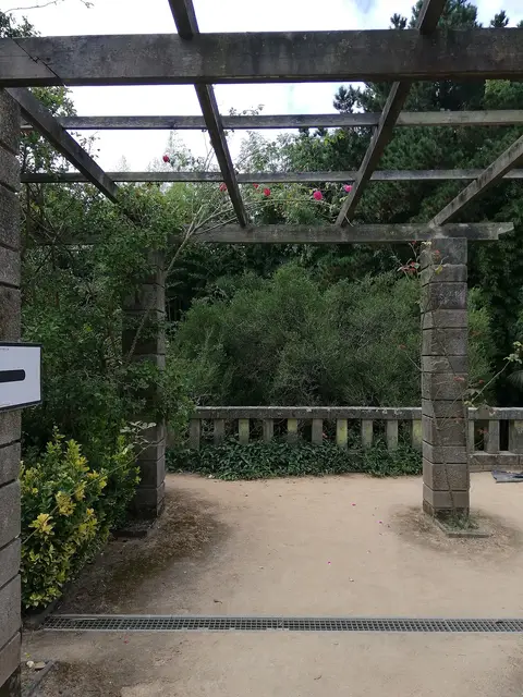 Pérgola de pedra e madeira com roseiras num jardim, sobre caminho de terra batida
