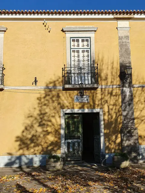 Fachada amarela do solar da Quinta da Fidalga, com varanda de ferro e porta de madeira antiga