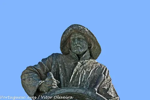 Pormenor da escultura O Homem do Leme, com chapéu e roda do leme, contra o céu azul