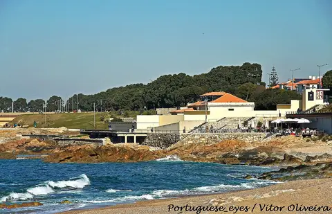 Praia do Homem do Leme, no Porto, com rochas, esplanada e edifícios junto ao mar