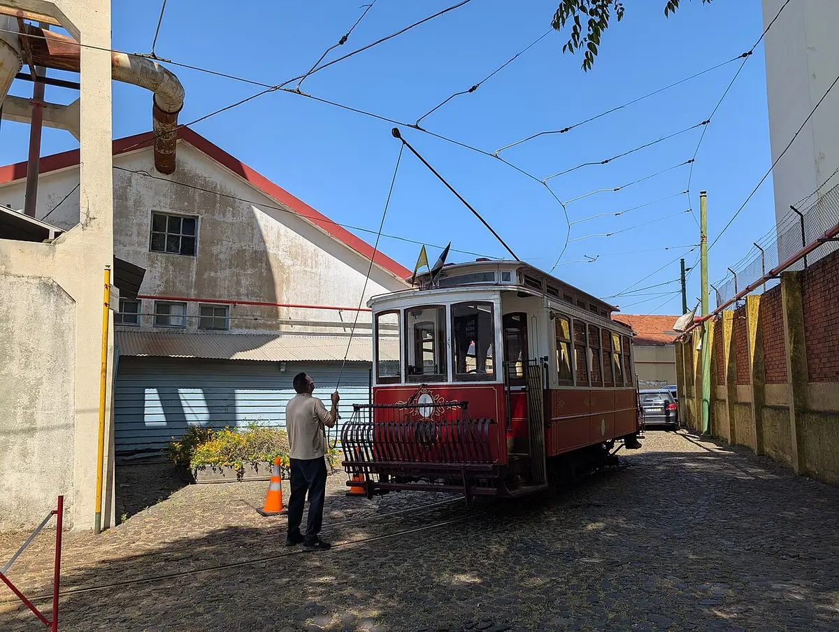 Elétrico antigo vermelho no exterior do Museu da Carris, com funcionário a ajustar o pantógrafo