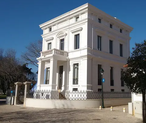 Fachada branca do palacete Casa Sommer, com varanda, gradeamento em ferro e céu azul