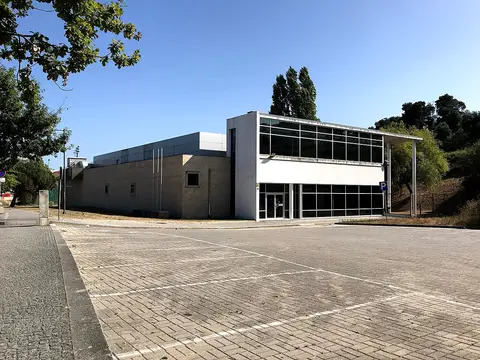 Exterior do edifício da piscina municipal, com fachada envidraçada e parque de estacionamento em frente