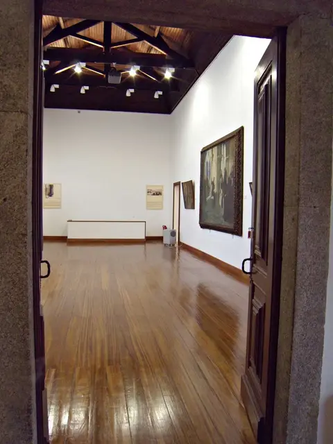 Sala de exposição da Casa Oficina António Carneiro, com soalho de madeira, tecto em vigas e pinturas nas paredes