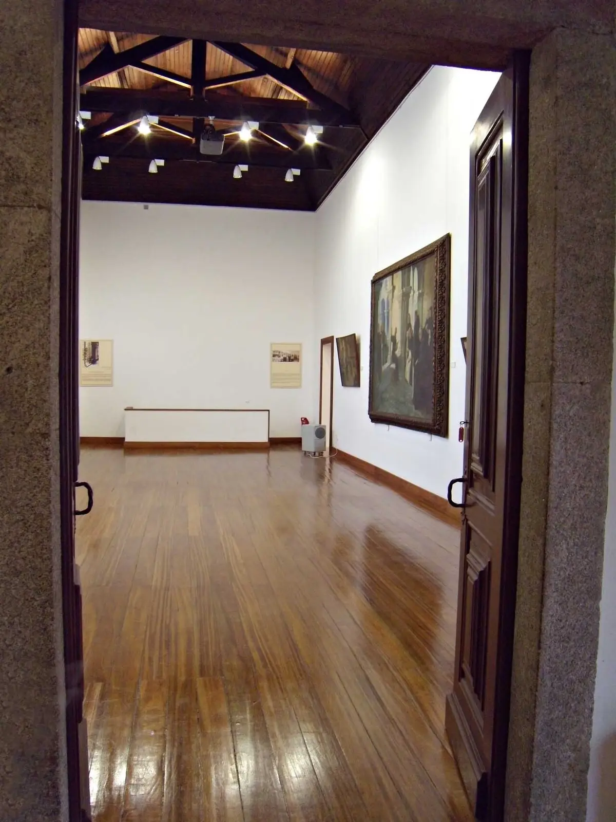 Sala de exposição da Casa Oficina António Carneiro, com soalho de madeira, tecto em vigas e pinturas nas paredes