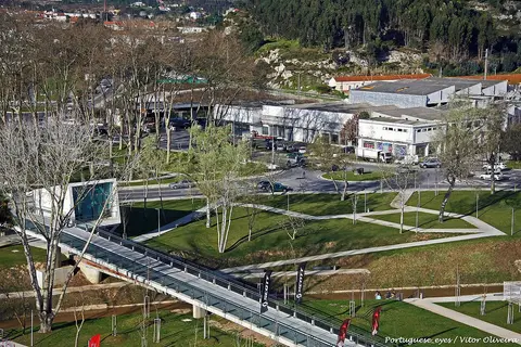 Vista elevada do parque urbano do Choupal, com passadiço sobre a ribeira, relvados e árvores