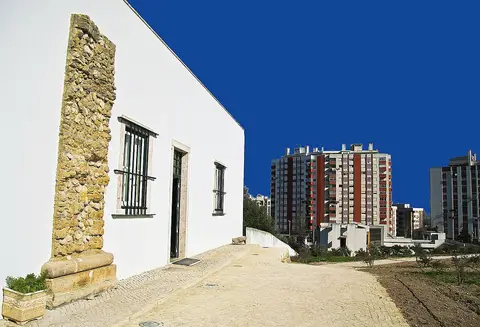 Edifício branco do palácio da Quinta Nossa Senhora da Piedade, com muro de pedra e prédios ao fundo