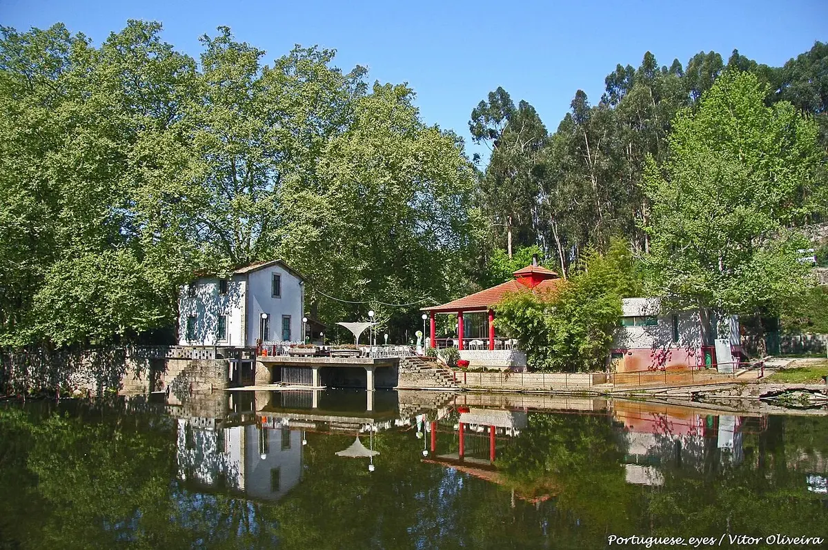 Parque das Termas de Vizela: casa branca e coreto vermelho refletidos no rio, rodeados de árvores.