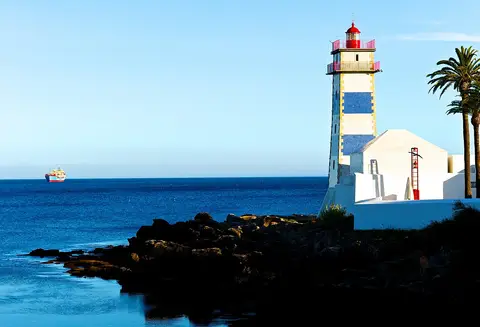 Farol de Santa Marta com azulejos azuis e brancos junto à costa rochosa em Cascais
