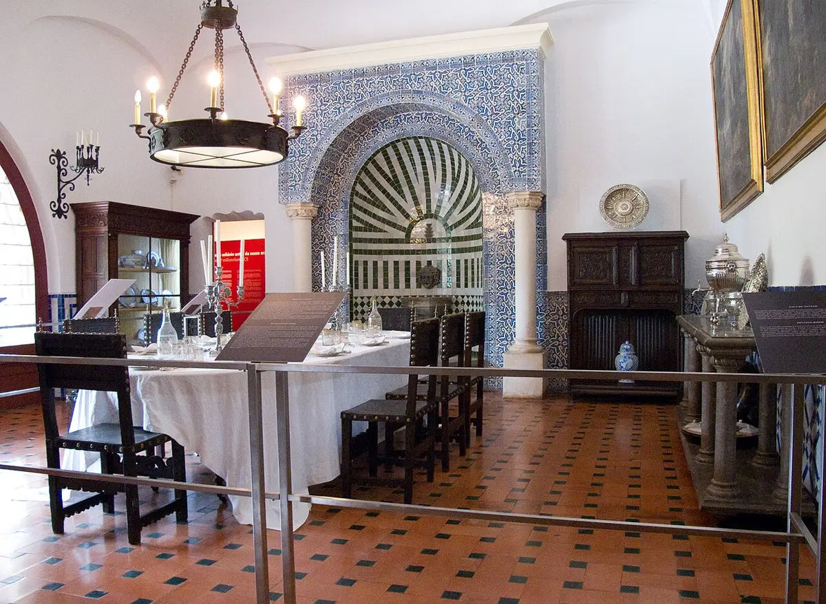 Sala de jantar do Museu Condes de Castro Guimarães com mesa posta, painel de azulejos e candeeiro de ferro