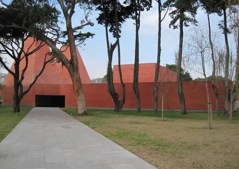 Edifício vermelho da Casa das Histórias Paula Rego, em Cascais, visto do jardim com árvores e caminho.