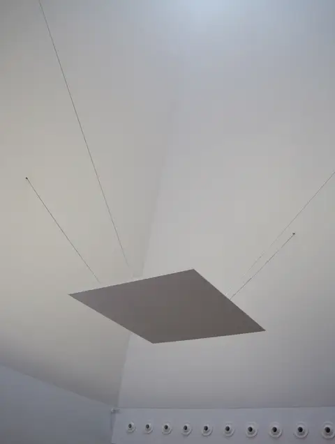 Pormenor do teto branco de uma sala da Casa das Histórias Paula Rego, com painel suspenso por cabos
