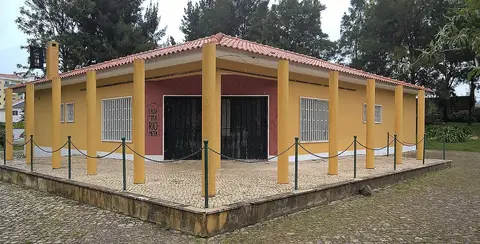 Edifício amarelo de um piso com colunas e telhado de telha, a Casa da Marioneta, rodeado por jardim