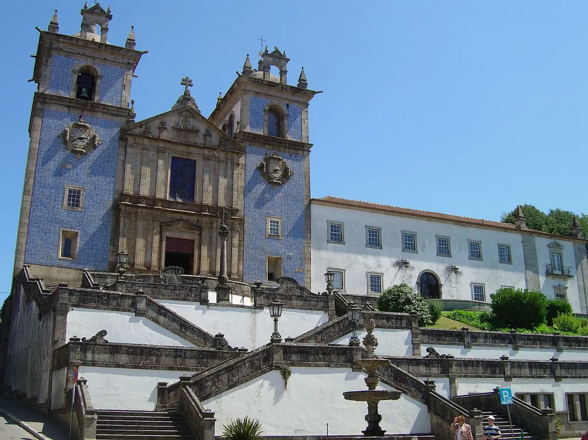 Igreja matriz com fachada azulejada e escadaria, ao lado do edifício branco do Convento dos Lóios