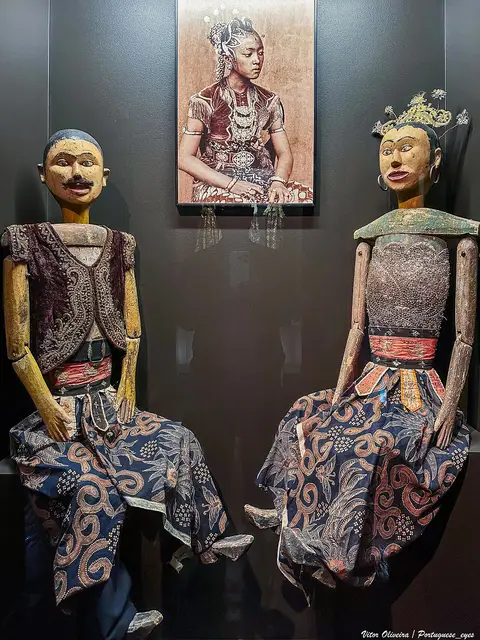 Duas marionetas de madeira com trajes tradicionais sentadas, em exposição no Museu da Marioneta
