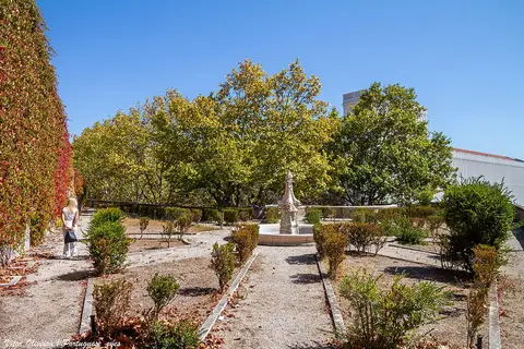 Jardim das Damas com canteiros de buxo, fonte de pedra central e árvores sob céu azul