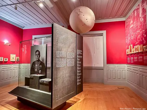 Sala de exposição com paredes vermelhas, globo suspenso e vitrina sobre a carreira diplomática