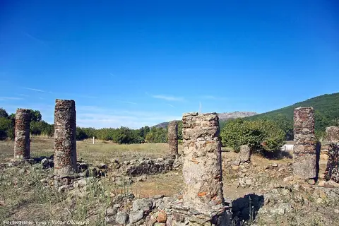 Ruínas da cidade romana de Ammaia com colunas de pedra e muros baixos, serra ao fundo