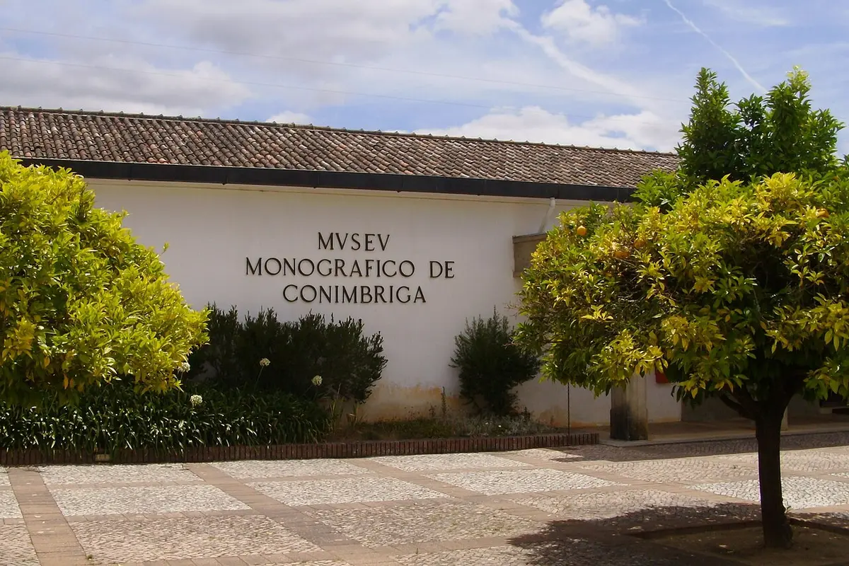 Fachada branca do Museu Monográfico de Conímbriga com letreiro e árvores em redor