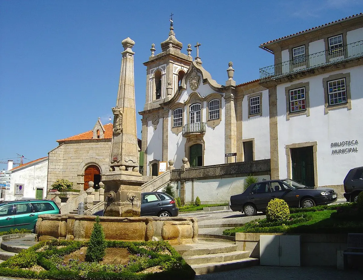 Edifício da Biblioteca Municipal de Seia junto a igreja barroca e chafariz de pedra em praça